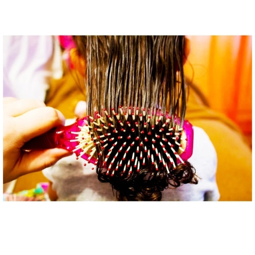 Person using a hairbrush with pins to style hair, with a blurred background